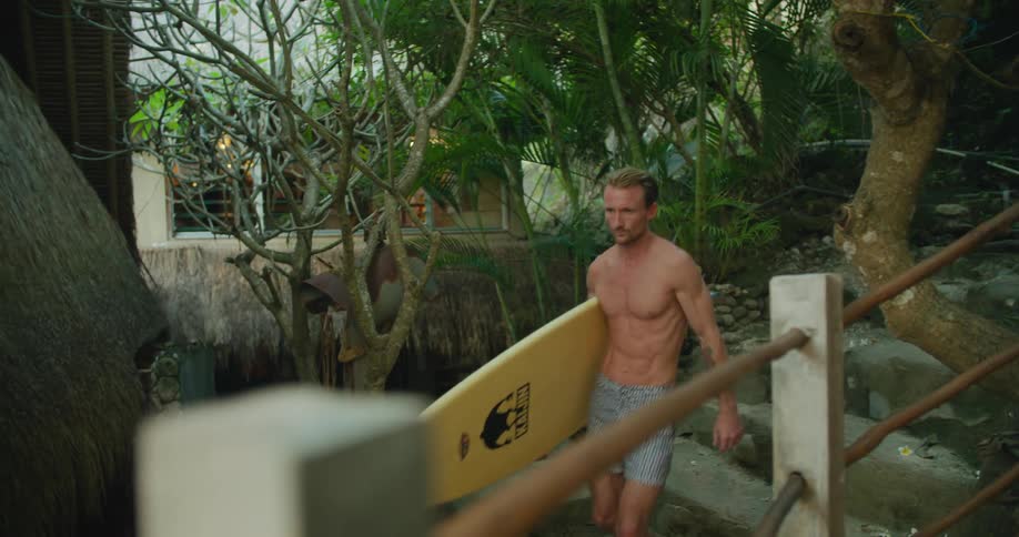 Man wearing shorts carries surfboard down outdoor steps