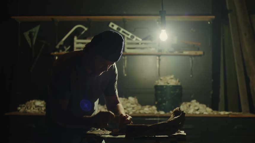 A man puts a piece of string in his mouth while working in a workshop