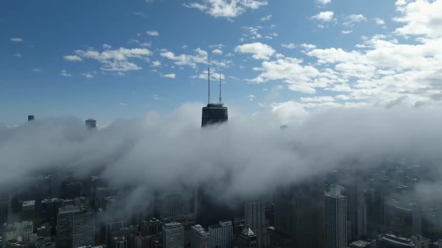 Aerial view of the skyline of a waterfront city covered in low white clouds at daytime