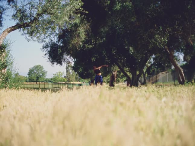 Woman moves through dance poses in fenced field under a clear sky