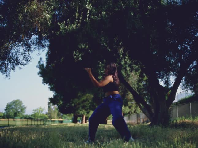 A teenage girl dances outside under trees