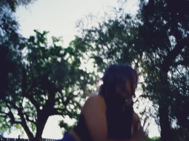 Female dancer with black top and blue pants dances in the garden next to trees
