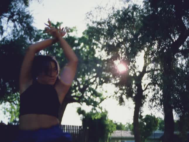 Young woman dances on the lawn in front of the trees in the backyard at evening