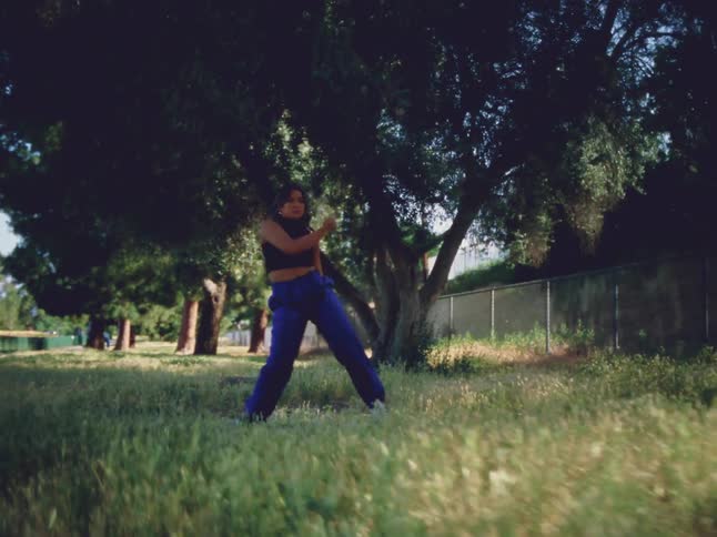 Female dancer with black top and blue pants dances in garden in the countryside