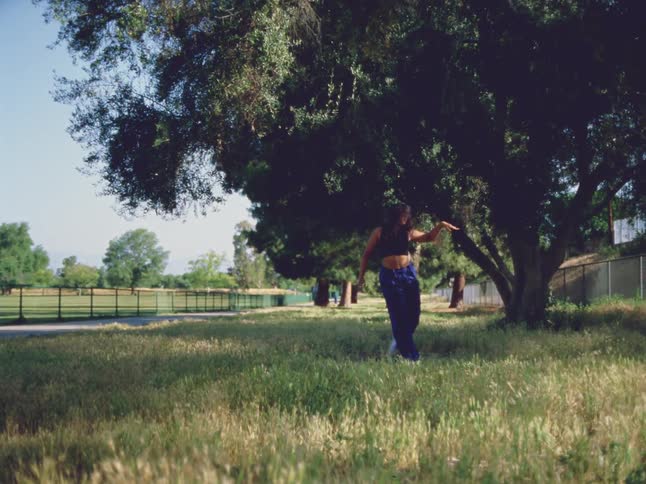 A woman dances in the grass near trees and a fence at the park