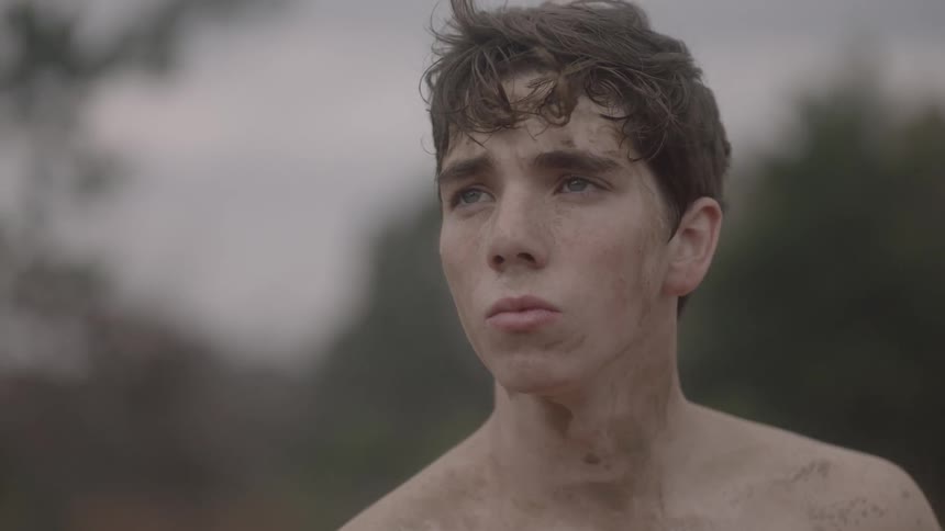 A dirty young man stands outside and looks onward