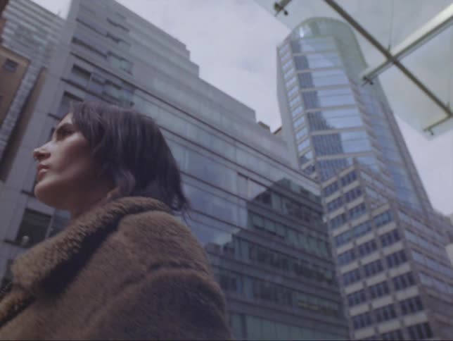 A woman walks past buildings and stores on a city street