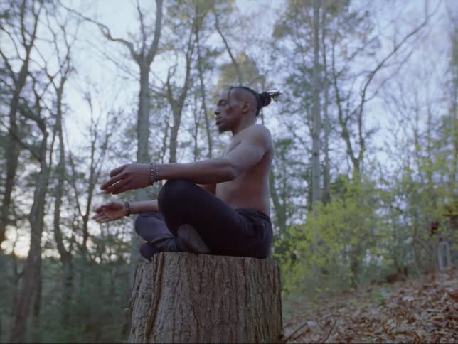A young black man is practicing meditation on a tree stump