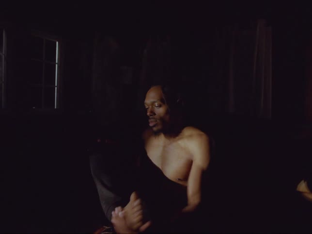 A man walks through a room full of shadows then sits down to meditate