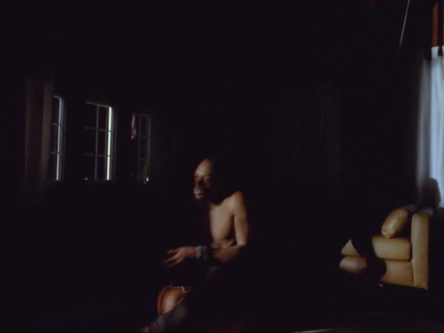 A man is sitting on a couch in a room at night time
