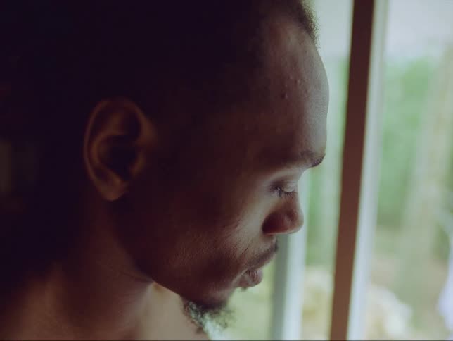 A man is sitting indoors and looking out a window in spring