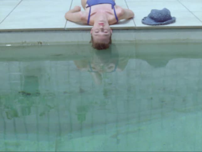 Woman wearing swimsuit lies on her back with her head touching the pool water and suddenly her eyes snap open