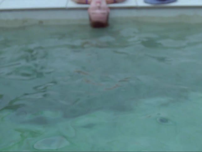 A woman is laying by the pool with her eyes closed and her head touching the water