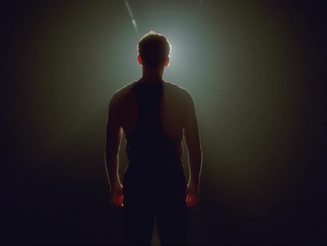 A man stands in front of a spotlight which brightens