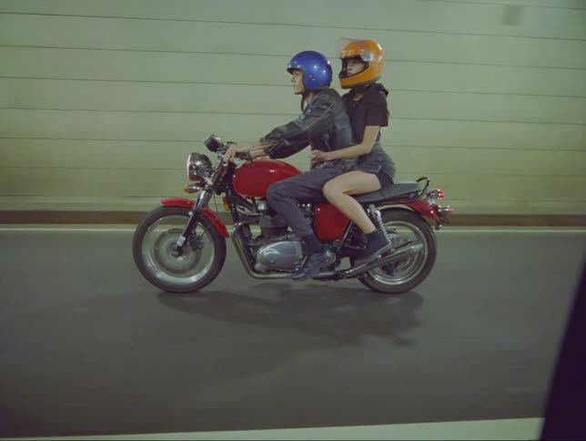 A man and woman ride a red motorcycle through a tunnel
