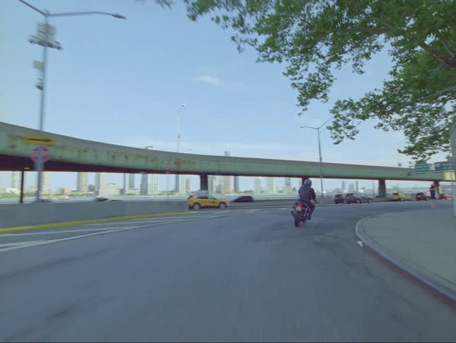 A motorcycle takes a curve to merge with highway traffic passing a woman walking on the sidewalk