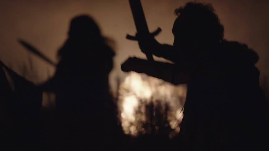 Men with swords running in a field near fire at night