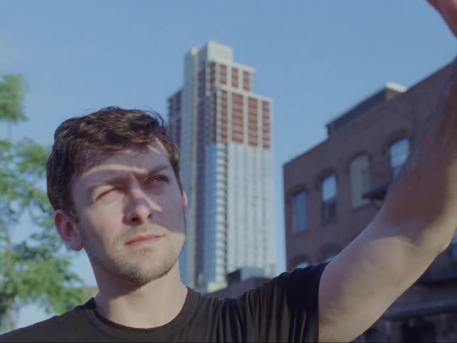A young white man is standing outside in the downtown area