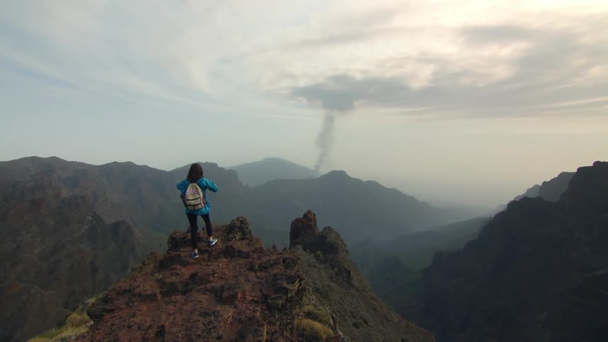 A woman hikes up to the top of a mountain and gets her camera out