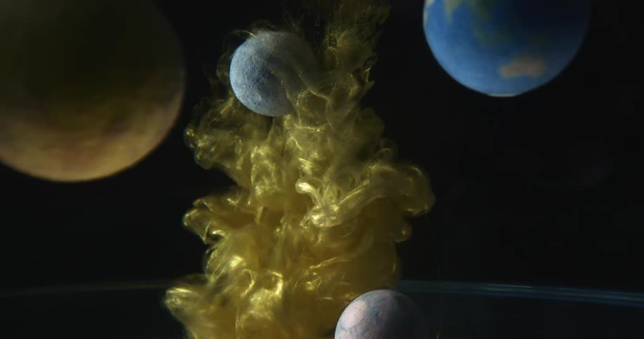 Bright gold liquid ink surround and cover small planets floating against a black background