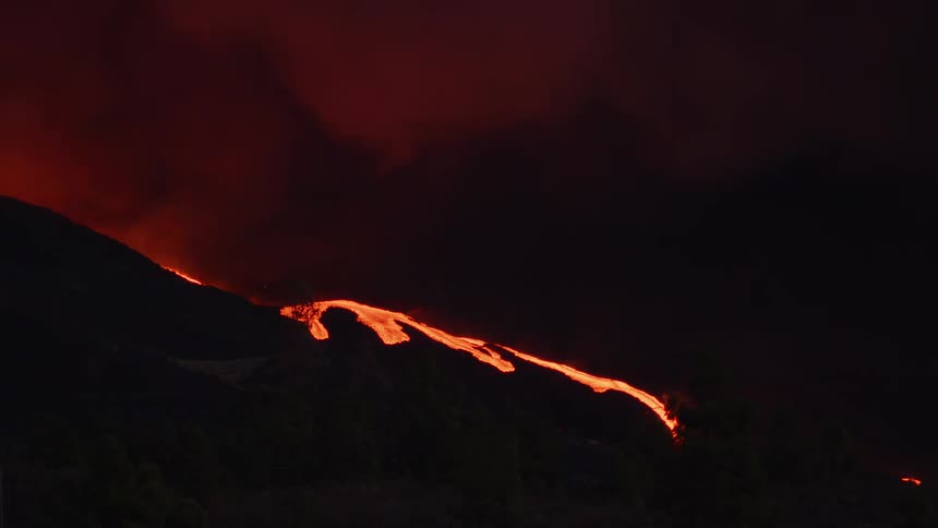 Red hot lava glows and illuminates the smoke as it flows out of a volcano