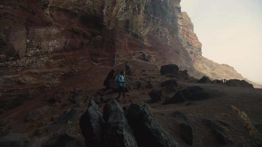 A woman carrying a camera walks up a rocky slope to the ledge of a mountain overlook