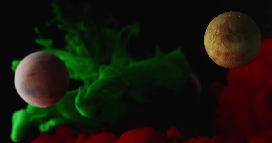 Bright green and red liquid ink surround and cover small planets floating against a black background