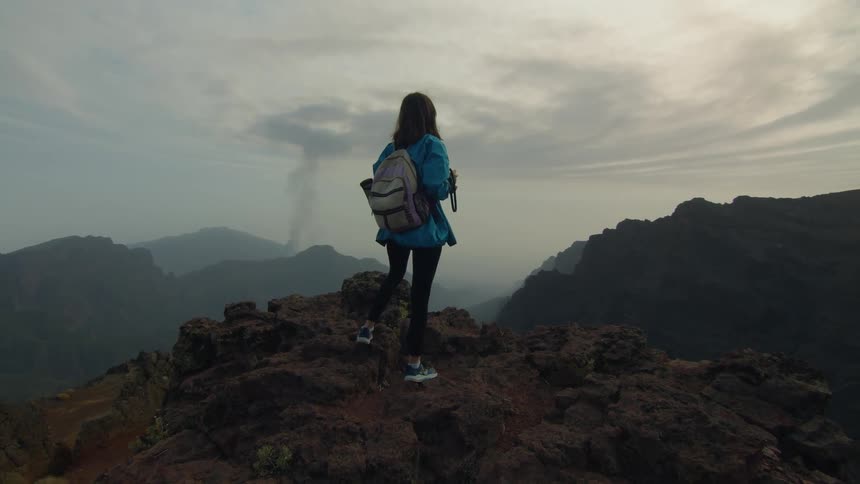 A teenage girl stands on a mountain and takes photos