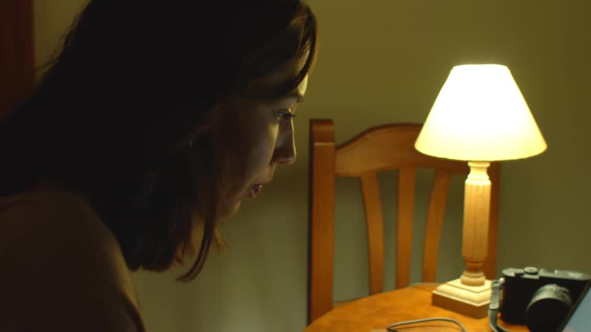 A woman sitting at her dining room table referencing a book while working on her laptop