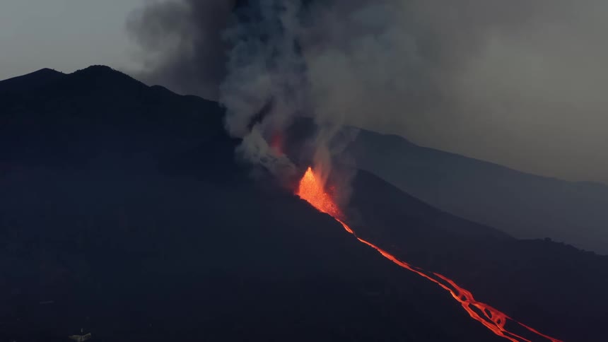 Red hot lava glows as it sprays and flows out of a volcano and smoke rises and fills the air