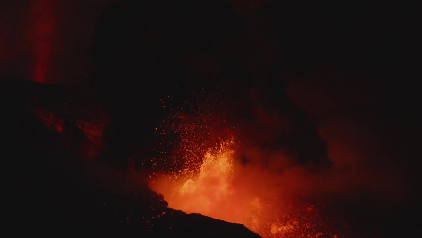 Molten lava is flying up into the air from the top of a volcano