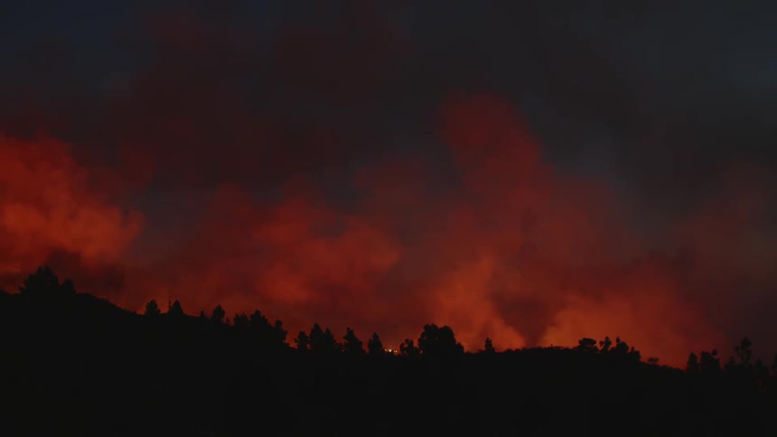 Smoke and the red glow of fire above the silhouette of a ridge at night