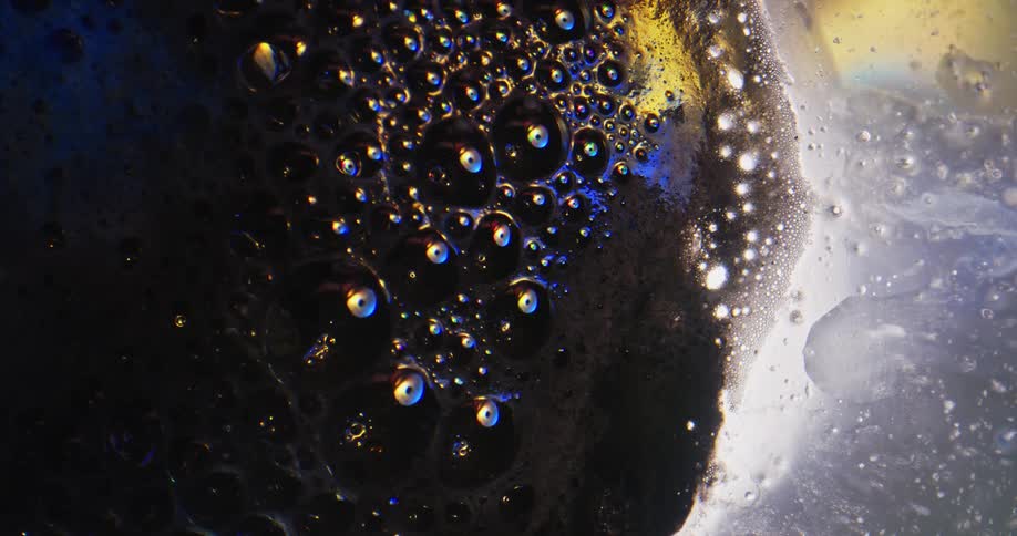 Bubbles are floating in a dark area and through yellow as they move to the white foam