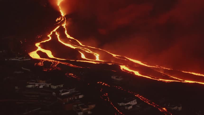 Molten lava is taking several paths down the side of a volcano towards a remote town