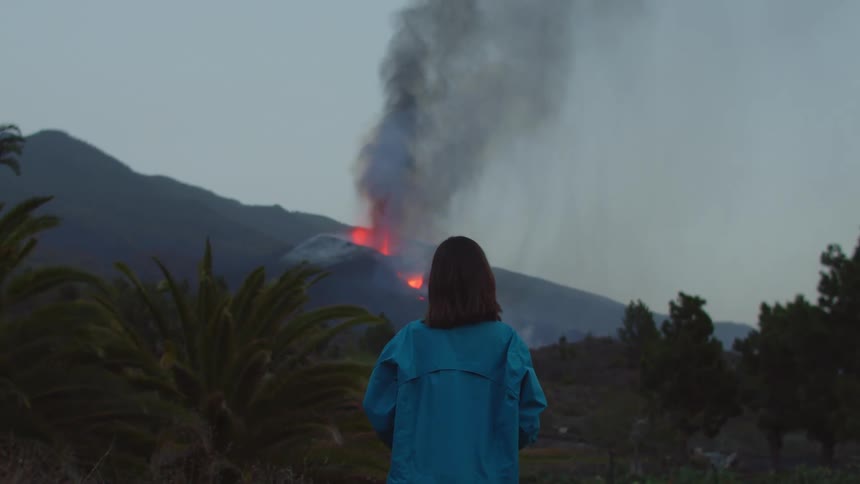 A girl stands and watches a volcano erupting