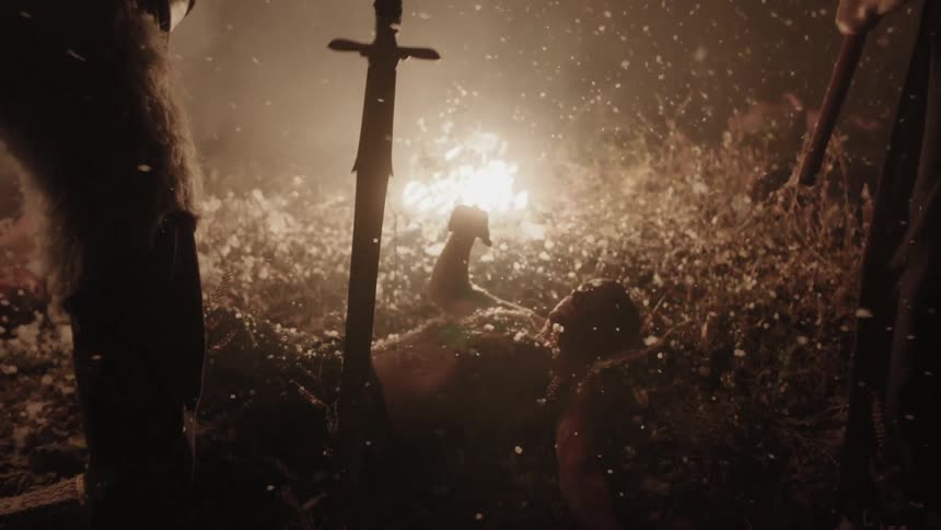 An injured man on the ground is stabbed by a sword at night
