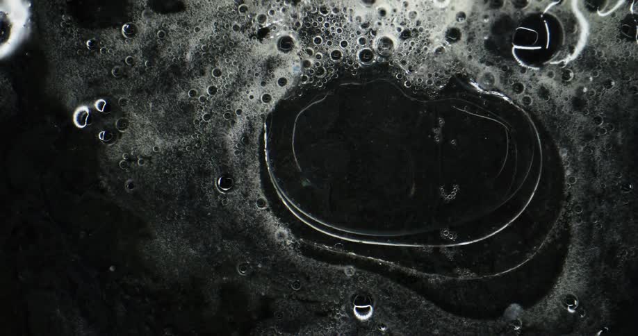 Bubble spheres are floating in a dark environment and a clear substance is expanding and pushing the bubbles outward
