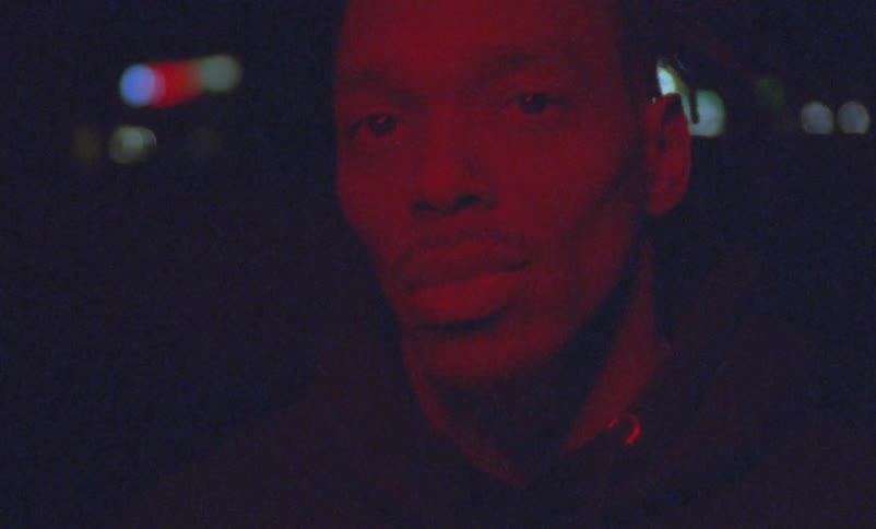 A man is looking around at night with red light flashing on his face