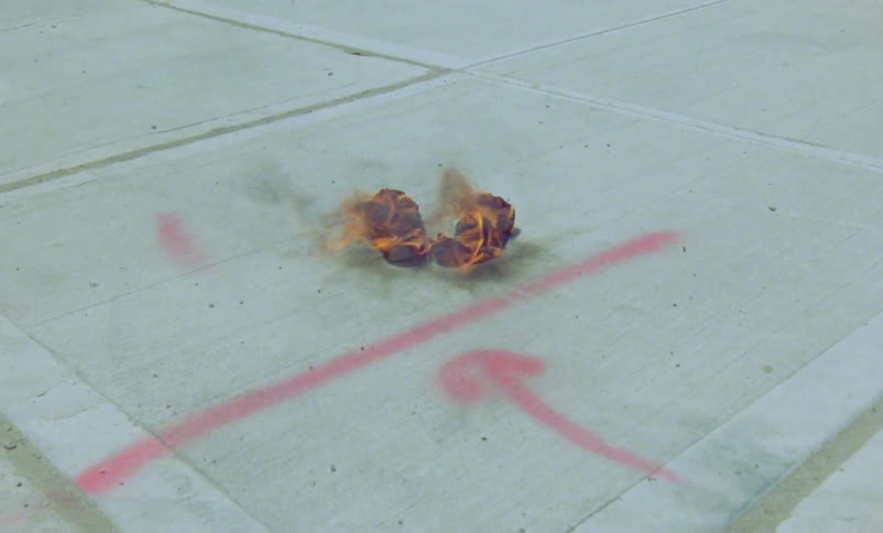 Shoes on a sidewalk burning in flames and there is graffiti painted on the walls