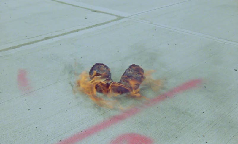 Pair of shoes on fire burning over the sidewalk in the city caught on vintage film