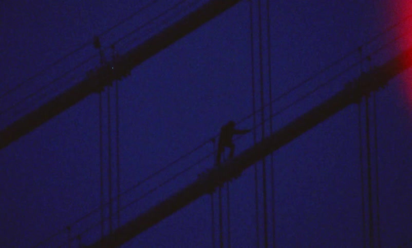 A person stands at the top of a suspension bridge hanging on to the sides