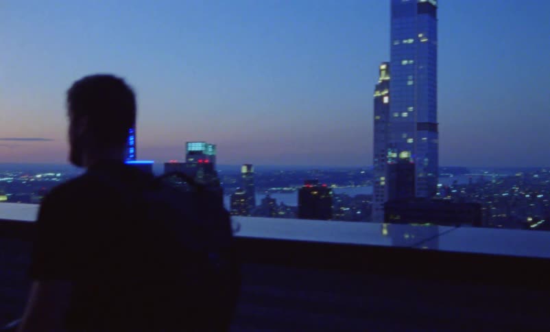 A group of photographers carrying cameras and equipment walk across a roof top to photograph the city skyline