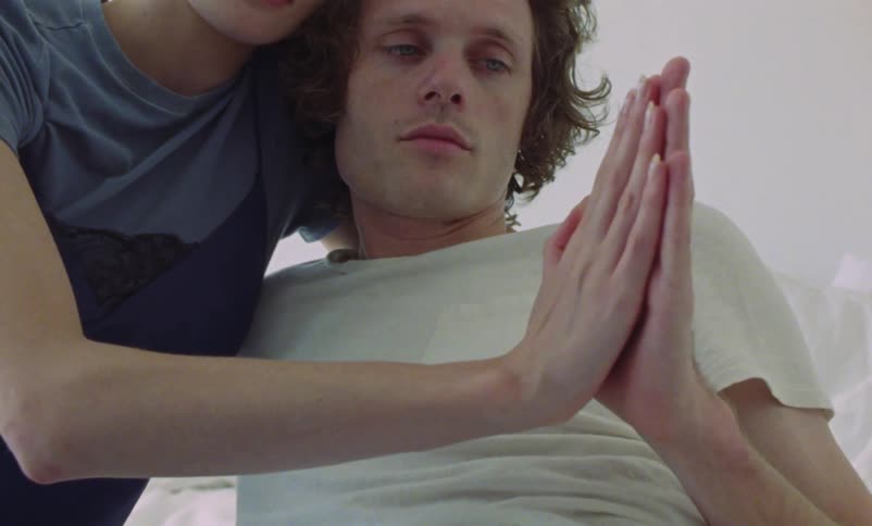 A man and woman are sitting on a bed with their hands pressed together