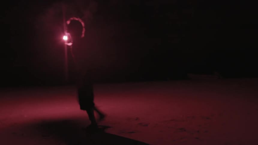 A man holding a flare as he walks along a beach at night