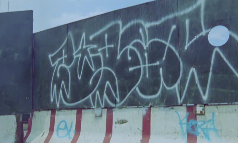 Shoes on a sidewalk are burning in flames and smoke floats into the sky high above the graffiti painted walls