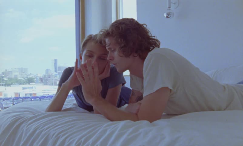 A man and woman are laying on a bed on their stomachs and holding hands