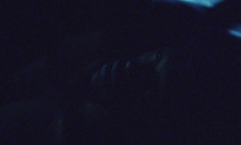 A man is lying in the darkness and he rubs his eyes with his hands