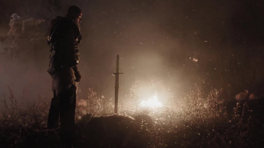 A man stands over the body of his enemy near a fire at night