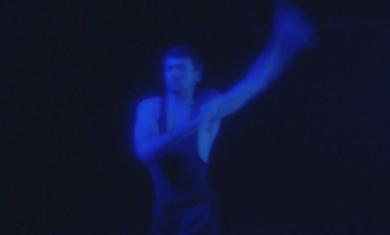 Male dancer performs on dark stage under bright blue colored lighting