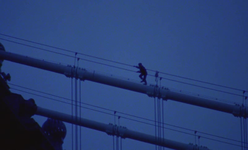 Silhouette of a person walking across the top of a suspension bridge as traffic moves below